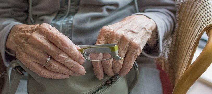 dettaglio delle mani di una donna anziana che tengono un paio di occhiali
