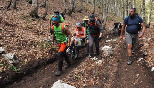 guide accompagnano disabile in montagna su una joelette