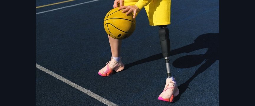 dettaglio delle gambe di una persona che indossa una protesi mentre sta palleggiando un pallone da basket su un campo sportivo 