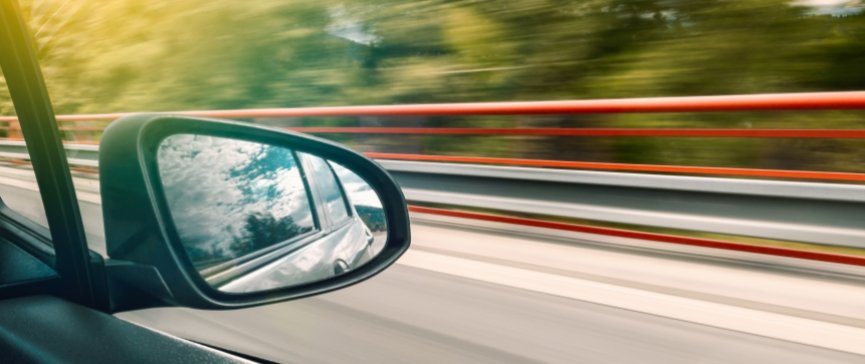 specchietto di un'auto e la strada affianco sfuocata