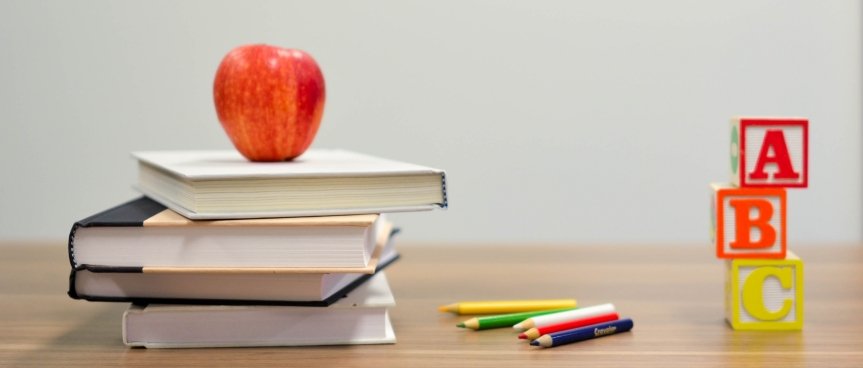 tavolo con sopra dei libri, una mela e delle matite colorate