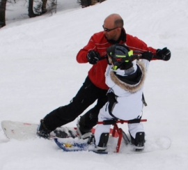 Bambino con difficoltà motorie che scia insieme al maestro