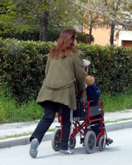 assistenza: una donna spinge una persona su sedia a rotelle 