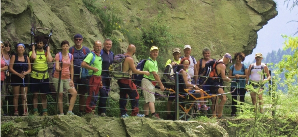 gruppo di persone, con disabilità e non, alle prese con un sentiero di montagna, protetti dal crepaccio da una ringhiera metallica