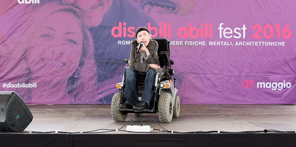 Maximiliano Ulivieri in carrozzina con un microfono in mano che parla sul palco del Disabili Abili Fest edizione 2016