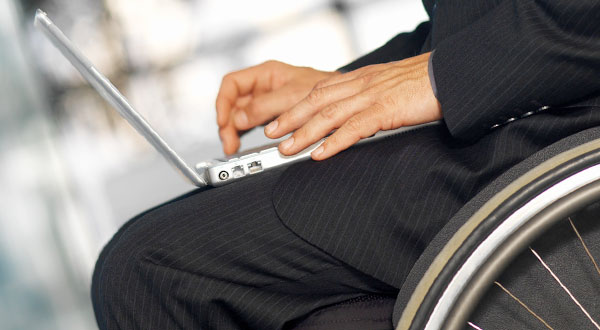 primo piano di mani al lavoro su un laptop poggiato sulle ginocchia di una persona in carrozzina