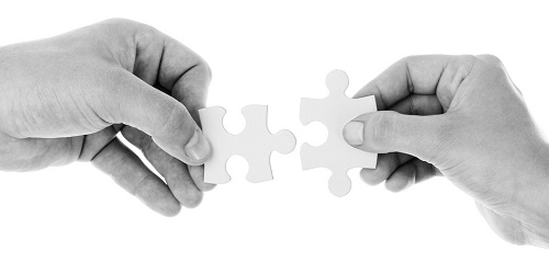 due mani che congiungono due pezzi di puzzle combacianti. Foto in bianco e nero.