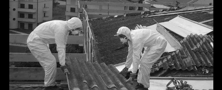 due lavoratori con tute integrali rimuovono amianto su un tetto