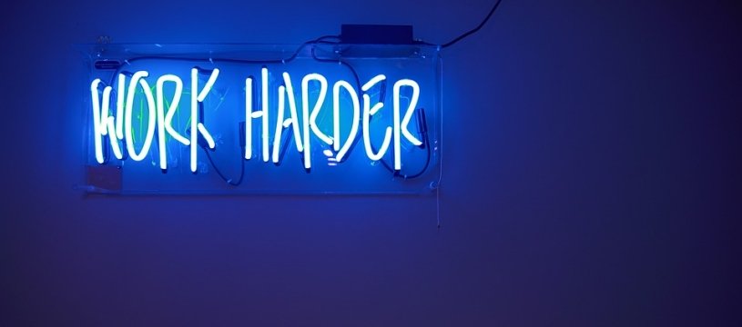 scritta al neon: work harder su muro di sfondo blu