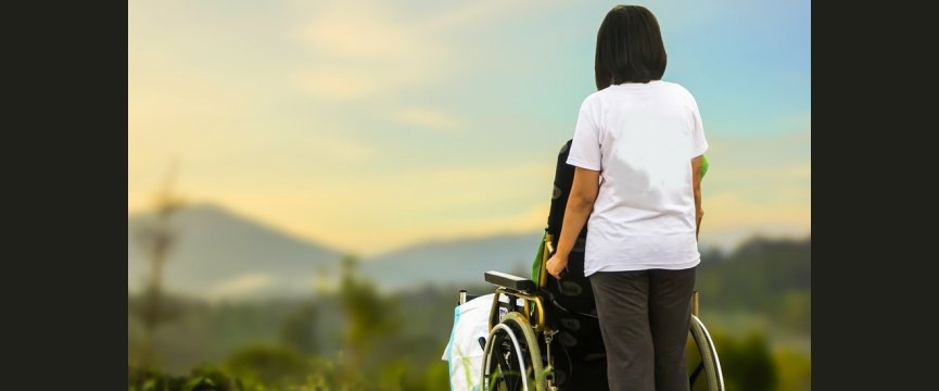 donna di spalle spinge una carrozzina per disabili