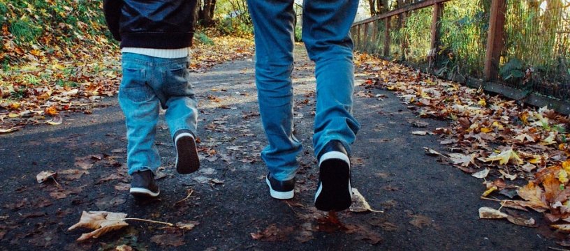 dettagli delle gambe di un bambino e papà di spalle mentre camminano in una strada piena di foglie gialle