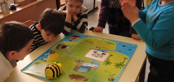 bambini di 7 o 8 anni attorno al banco di scuola che giocano con un'apina robotizzata