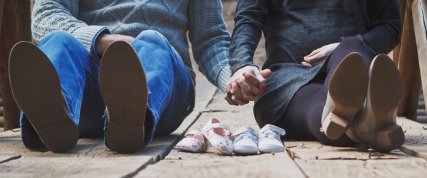 un uomo e una donna seduti per terra si tengono per mano con scarpette in mezzo