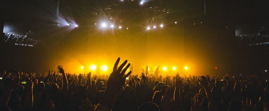 dettaglio delle mani alzate di alcuni spettatori di un concerto. sullo sfondo, il palco