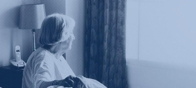 donna anziana seduta su un letto guarda fuori dalla finestra 