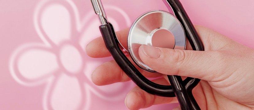 mano di una donna che tiene uno stetoscopio, su uno sfondo rosa