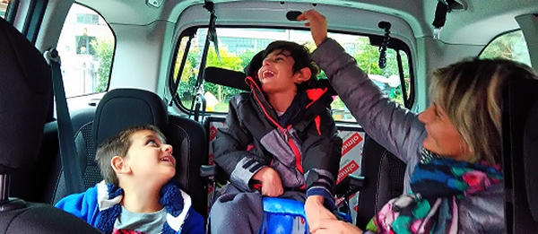 una mamma accarezza suo figlio disabile in auto con a fianco il fratellino: il caricamento in auto è stato effettuato con un allestimento by Olmedo