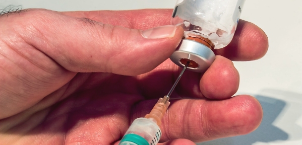mani di uomo impegnate a riempire una siringa con un medicinale contenuto in una boccetta di vetro