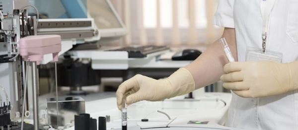 dettaglio delle mani di una persona che indossa guanti in lattice e armeggia con provette in un laboratorio analisi 