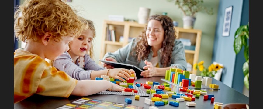 due bambini, tra cui una cieca, giocano vicino a una donna con i mattoncini lego braille sparsi sul tavolo