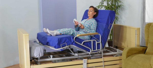 signora anziana stesa a letto che sta inclinando il letto con un telecomando per alzare gambe e torso 