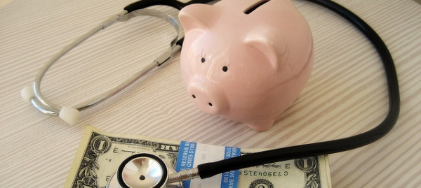 salvadanaio a forma di porcellino, banconote e stetoscopio appoggiate su un tavolo