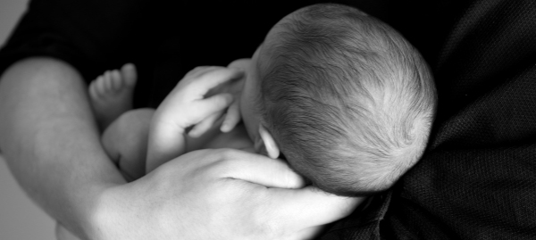 immagine in bianco e nero di un neonato tenuto in braccio da uno dei genitori di cui si vede solo la mano e parte dell'avambraccio
