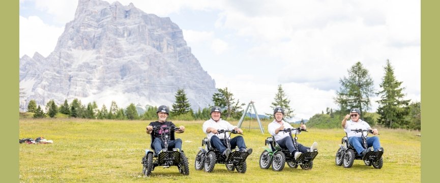 su un pianoro con montagne alle spalle, quattro persone a bordo di Zoom il quad per disabili 
