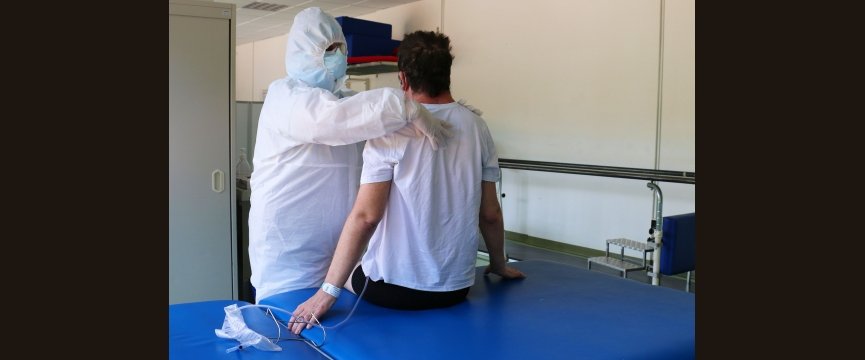 sanitario esegue esercisi di riabilitazione su un paziente, indossando tuta e dispositivi di protezione personali
