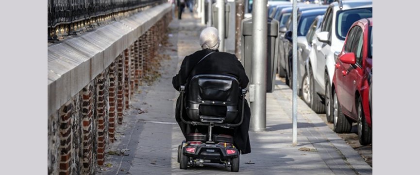 signora anziana di spalle a bordo di uno scooter si un marciapiede 