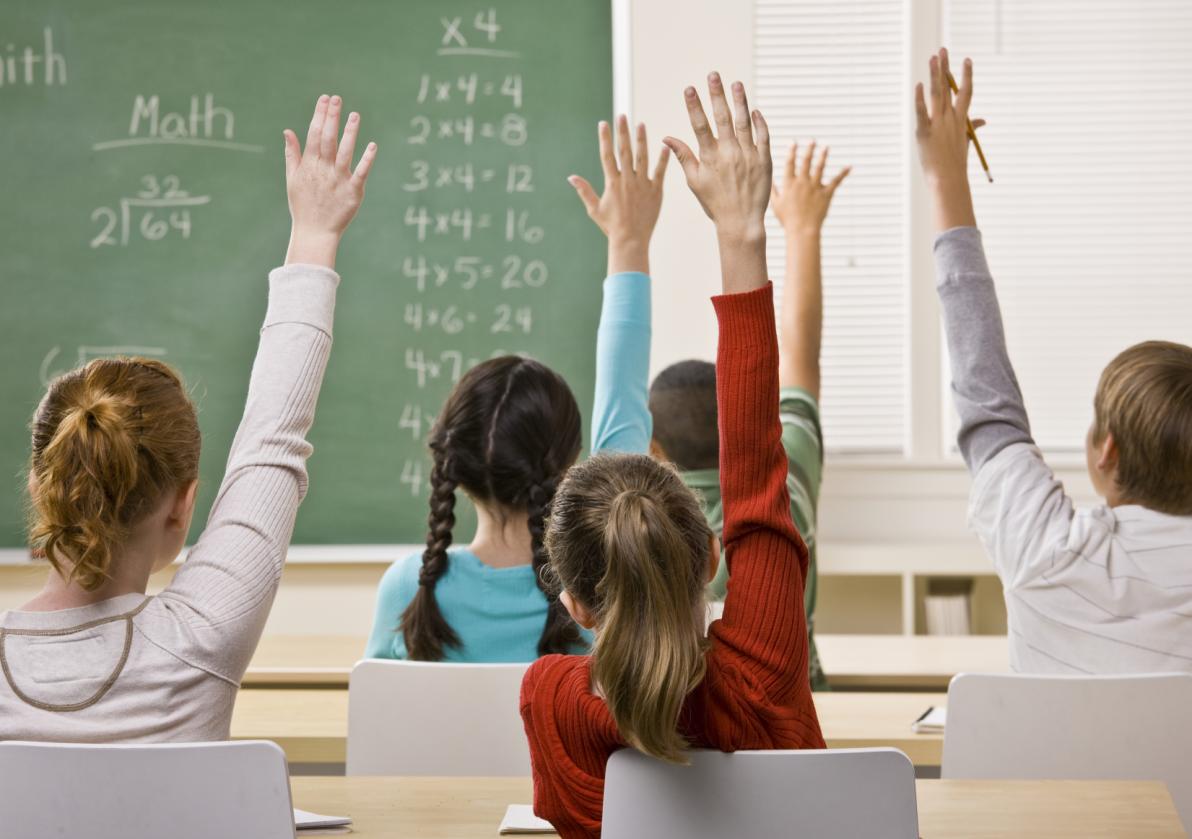 bambini di spalle con le mani alzate in classe