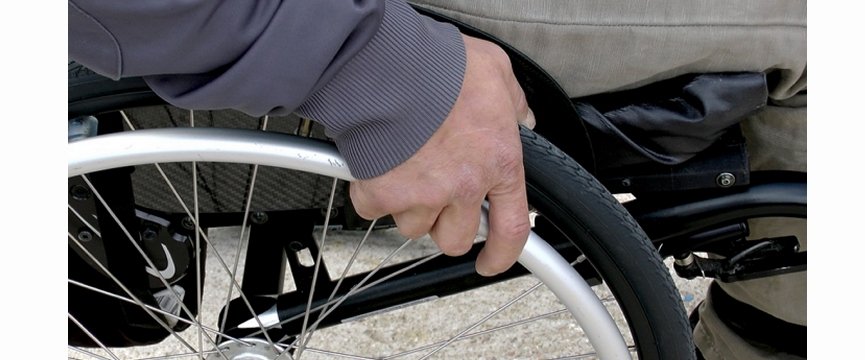 dettaglio di una mano sulla ruota di una carrozzina per disabili