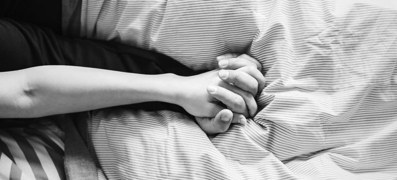 dettaglio delle mani avvinghiate di due persone in mezzo alle lenzuola di un letto