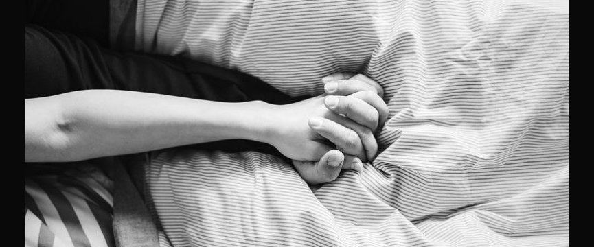 dettaglio delle mani intrecciate di due persone su un lenzuolo stropicciato