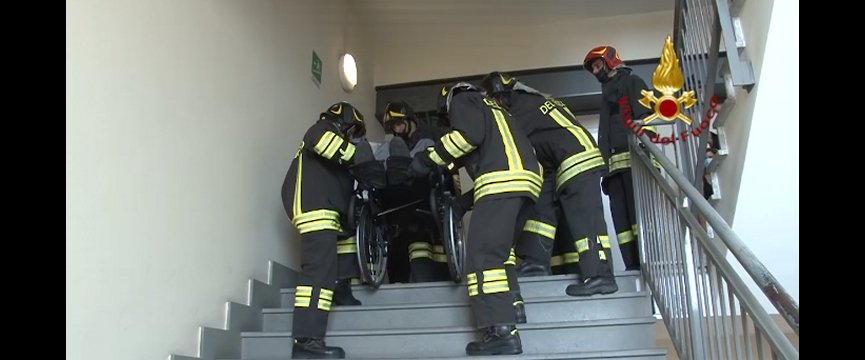 vigili del fuoco trasportano giù per le scale un uomo in carrozzina