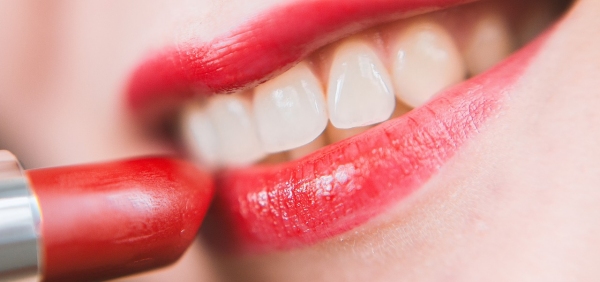primo piano di labbra di donna sorridente che applica un rossetto rosso 