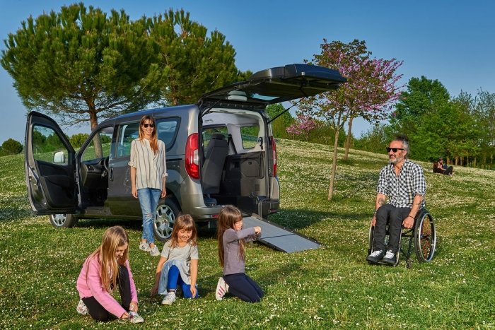 famiglia con papà in carrozzina su un prato vicino al Fiat Doblo F Style One