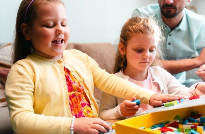 due bambine, tra cui una cieca, davanti ad mucchietto di mattoncini lego braille ciechi