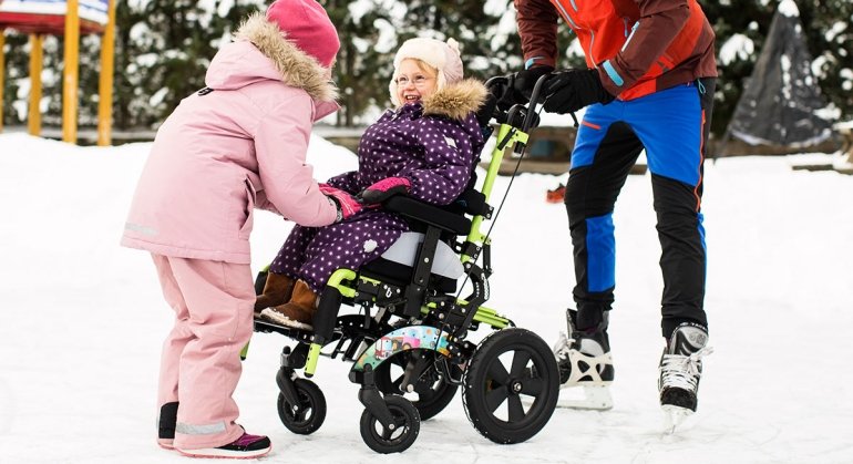 bambina su carrozzina Neatech Levia Basculante sulla neve vicino a due adulti