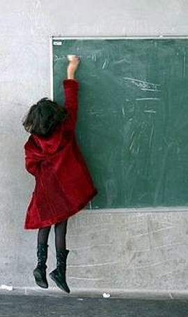 scuola: bambina di spalle scrive alla lavagna 