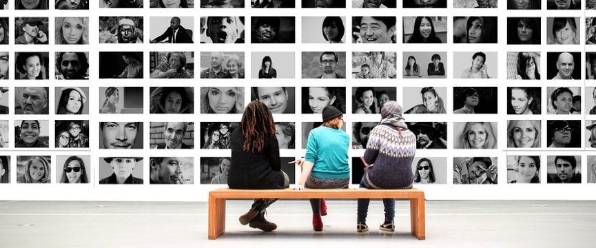 tre ragazzi seduti su una panchina di spalle che guardano una parete piena di foto