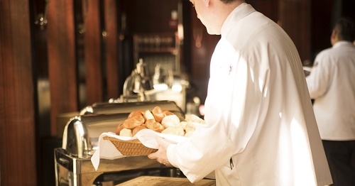 persona di spalle con camicia bianca che ha in mano un cesto di pane